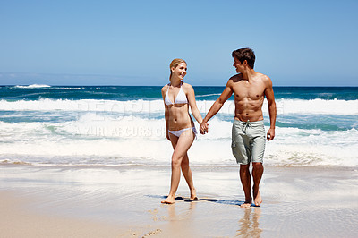 Buy stock photo Shot of a happy young couple enjoying a romantic walk on the beach