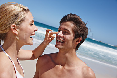 Buy stock photo Shot of a happy young woman applying sunscreen to her boyfriend's nose at the beach