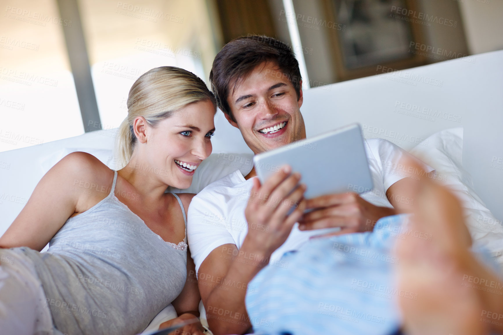 Buy stock photo Shot of a happy couple lying in bed and using a digital tablet together