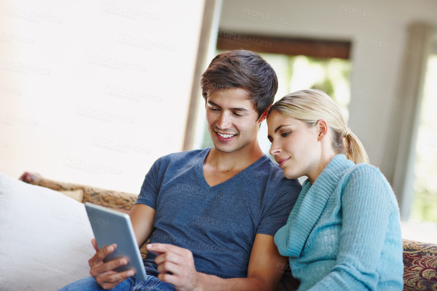 Buy stock photo Shot of a happy young couple using a digital tablet together on the sofa at home