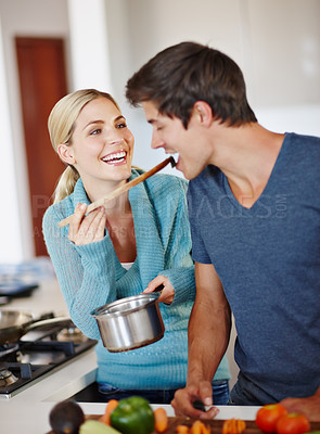Buy stock photo Shot of a beautiful young woman giving her husband a taste of her cooking