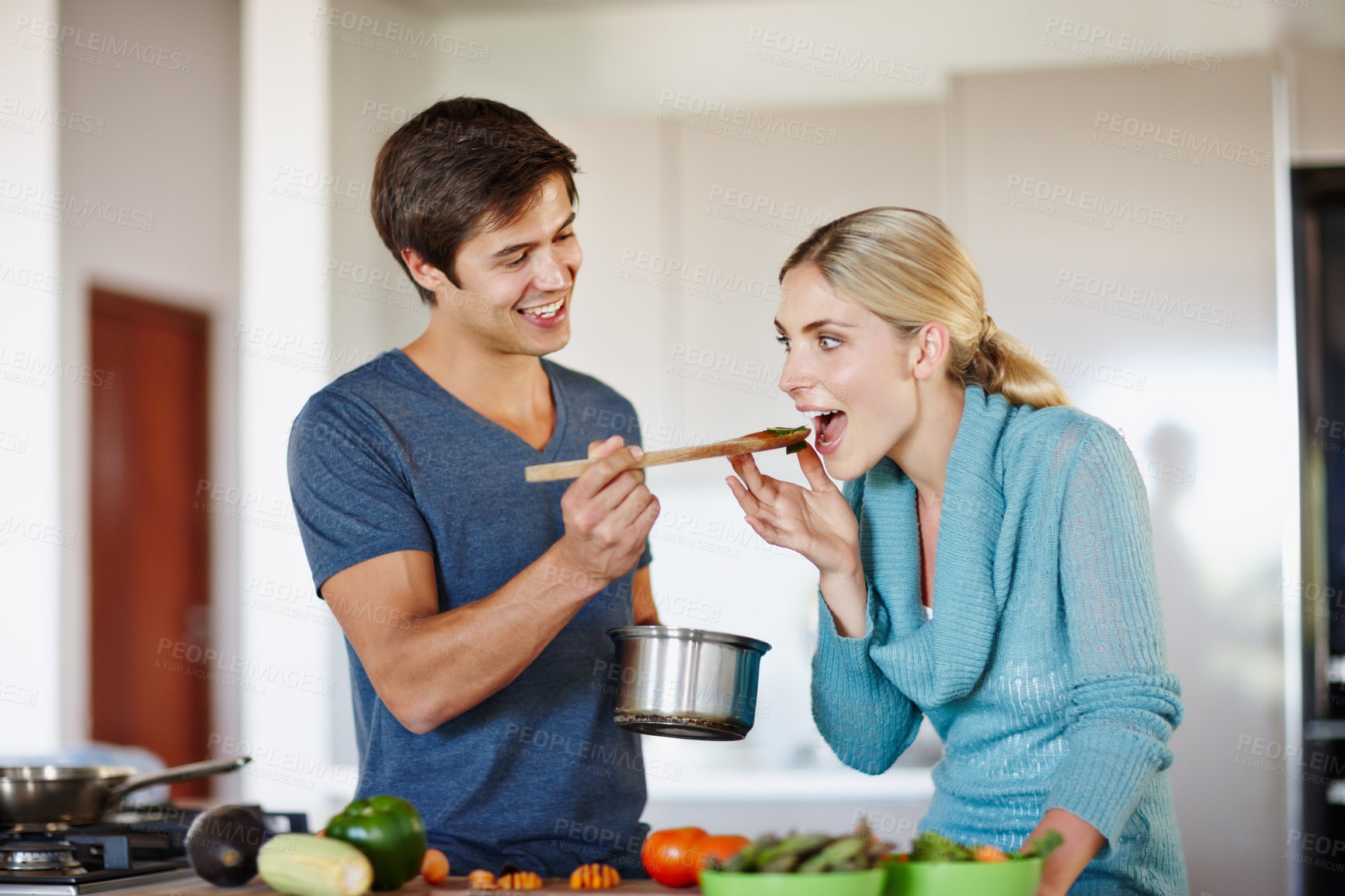 Buy stock photo Shot of a handsome young man giving his wife a taste of his cooking