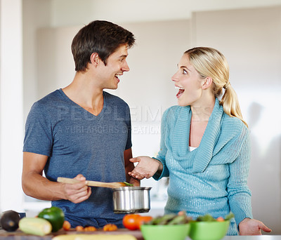 Buy stock photo Shot of a handsome young man giving his wife a taste of his cooking
