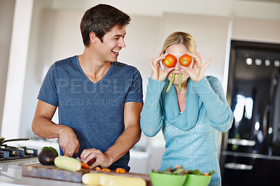 Buy stock photo Shot of a playful young woman making funny faces with vegetables while her husband prepares a meal 
