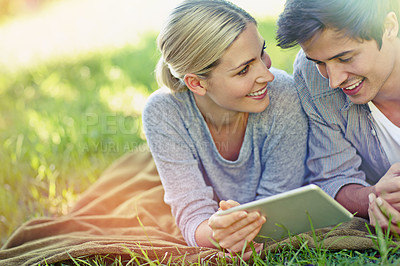 Buy stock photo Shot of a happy young couple lying on the grass and using a digital tablet together