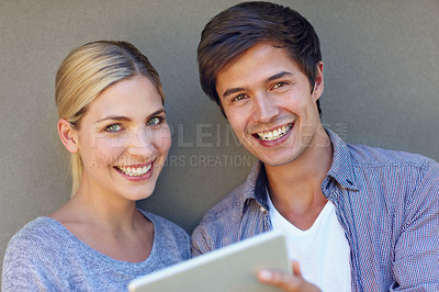Buy stock photo Portrait of a happy young couple using a digital tablet together against a gray background