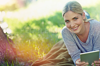 Buy stock photo Portrait of a beautiful young woman lying on the grass and using a digital tablet 