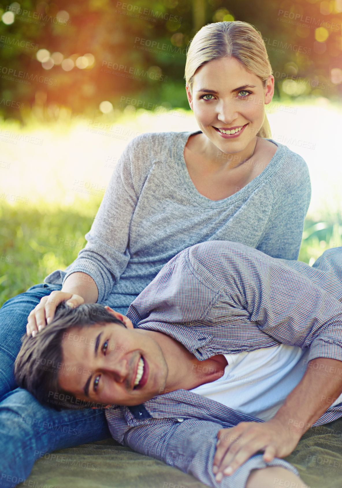 Buy stock photo Shot of a happy young couple lying on the grass and sharing an affectionate moment together