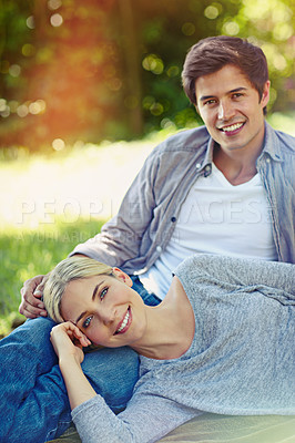Buy stock photo Shot of a happy young couple lying on the grass and sharing an affectionate moment together