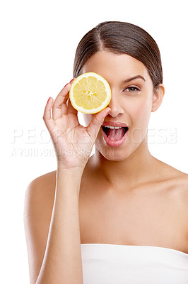 Buy stock photo Studio portrait of an attractive young woman holding up half a lemon in front of her eye