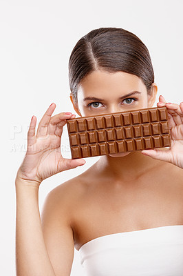 Buy stock photo Studio portrait of an attractive young woman holding a bar of chocolate in front of her mouth