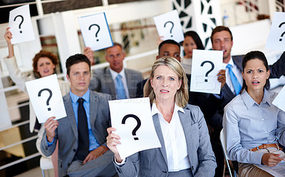 Buy stock photo Shot of a group of businesspeople holding up signs with question marks on them during a work presentation 
