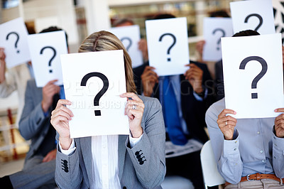 Buy stock photo Shot of a group of businesspeople holding up signs with question marks on them during a work presentation 
