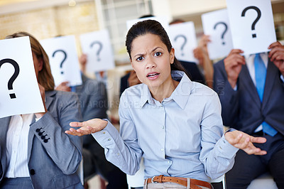 Buy stock photo Shot of a group of businesspeople holding up signs with question marks on them during a work presentation while their colleague looks confused