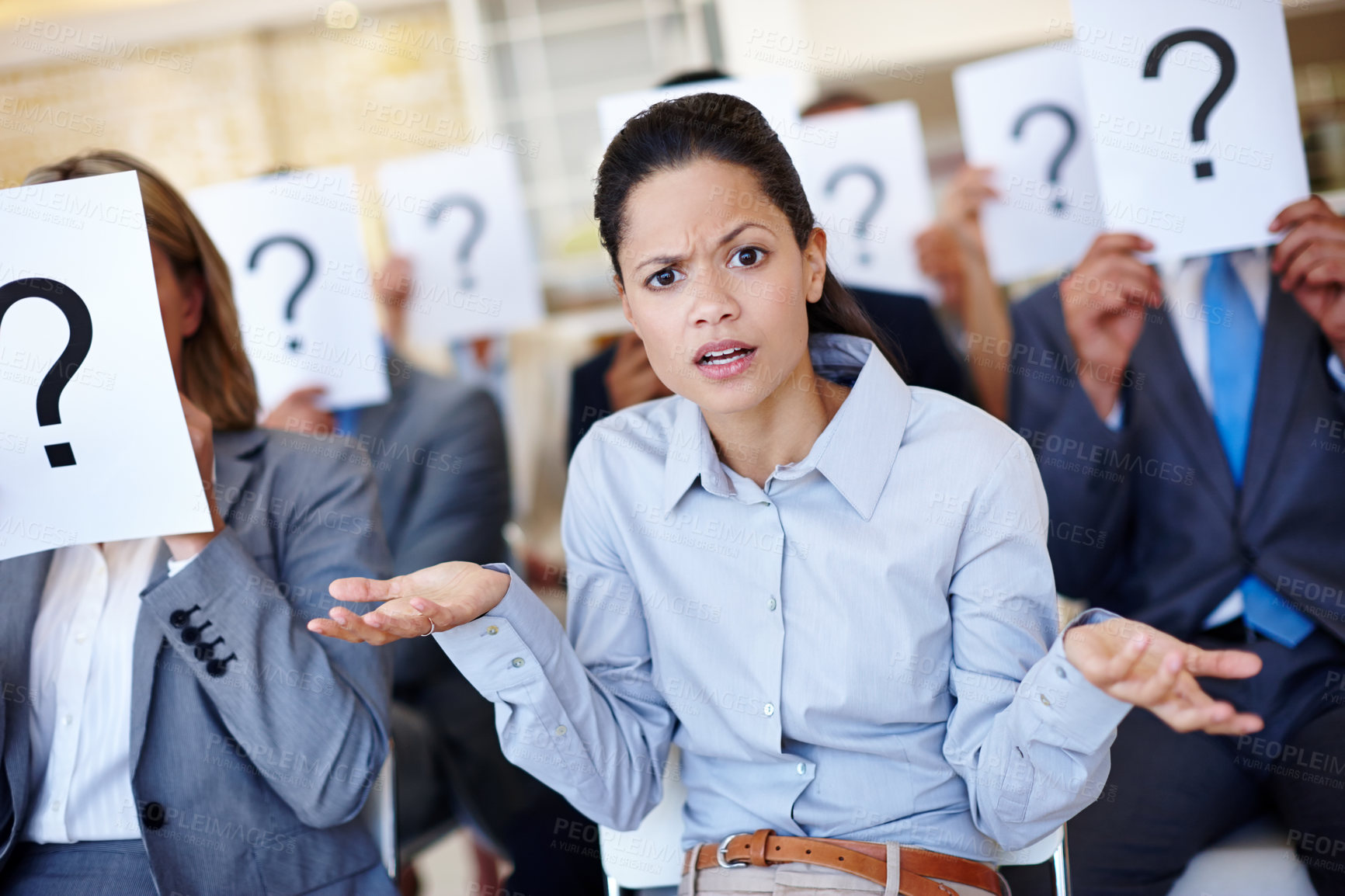 Buy stock photo Shot of a group of businesspeople holding up signs with question marks on them during a work presentation while their colleague looks confused