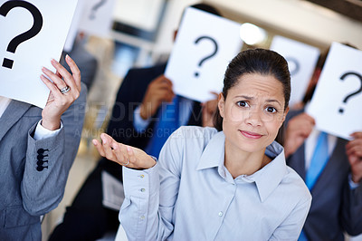 Buy stock photo Shot of a group of businesspeople holding up signs with question marks on them during a work presentation while their colleague looks confused