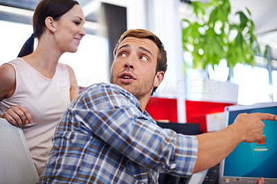 Buy stock photo Shot of a male designer sitting at his computer and pointing out something to a colleague