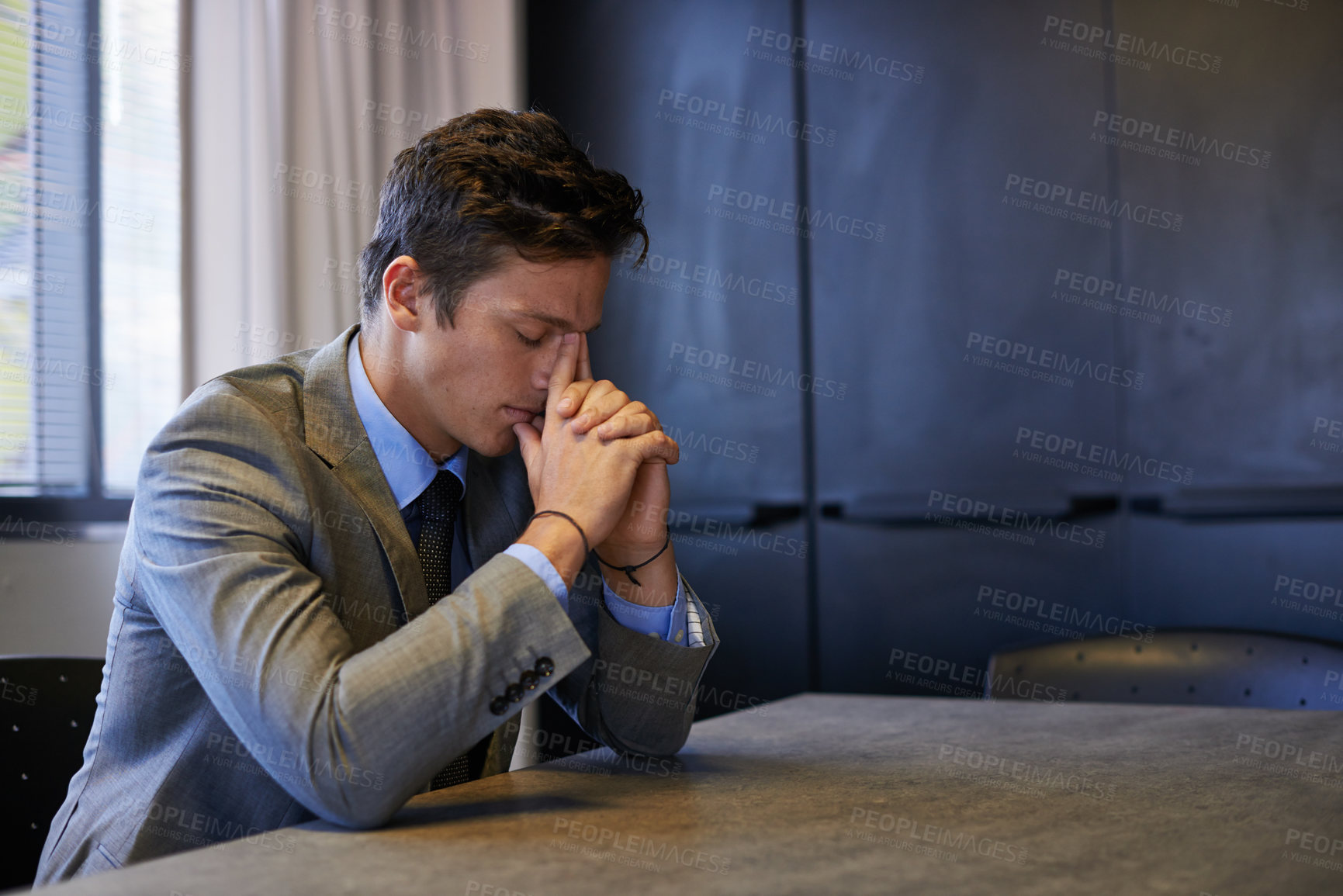 Buy stock photo A young businessman looks tired and stressed while sitting at his desk. Depressed tired businessman sitting in the office feeling lonely, massaging his forehead suffering from burnout at work
