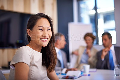 Buy stock photo A young businesswoman sitting at a conference table with her colleagues discussing work in the background