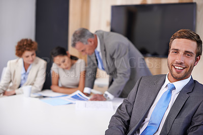 Buy stock photo A young businessman sitting at a conference table with his colleagues in the background