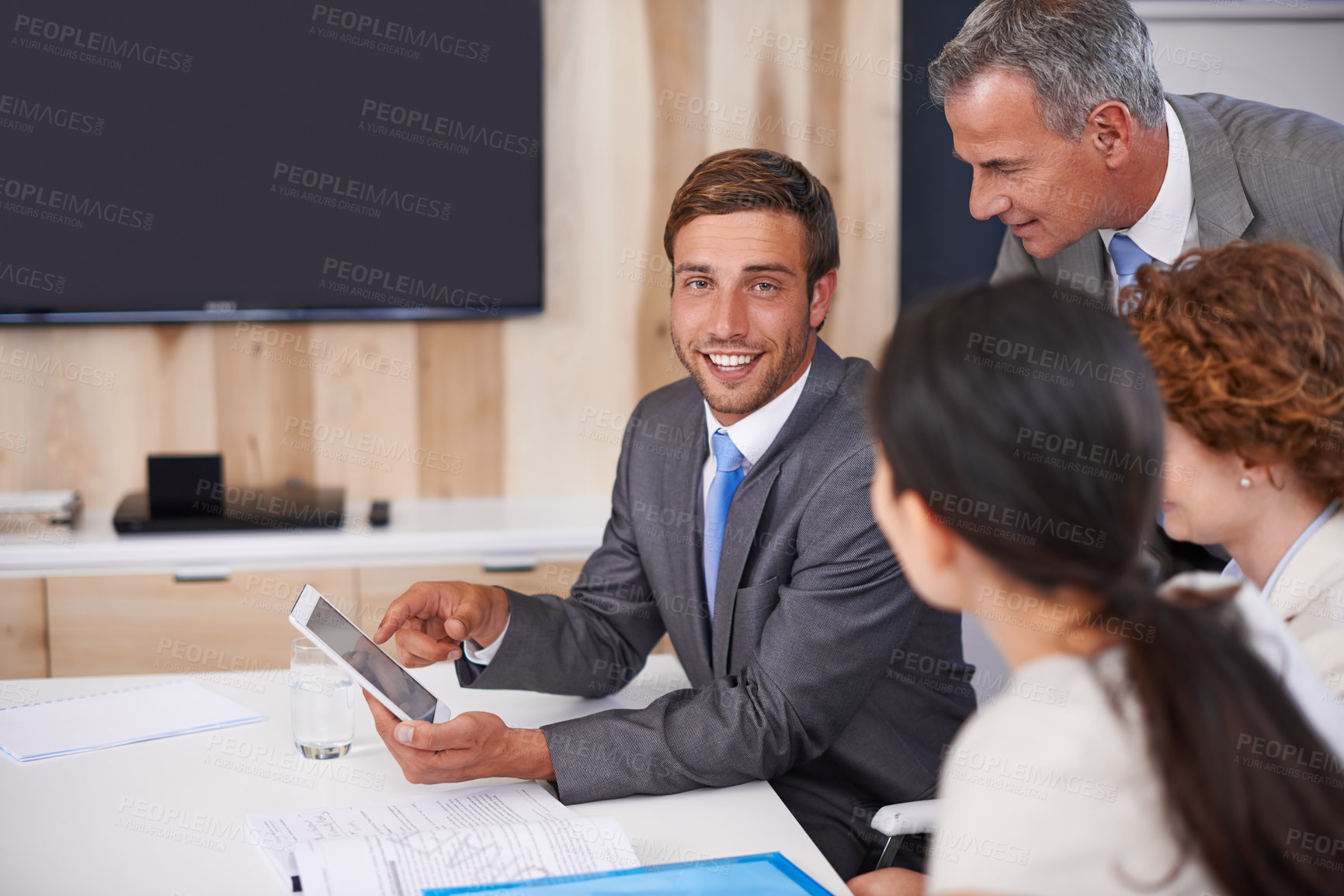 Buy stock photo Shot of a young businessman using a tablet in a meeting with his colleagues