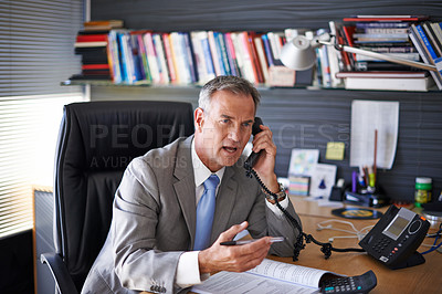 Buy stock photo Shot of a mature businessman looking displeased while talking on the phone in his office