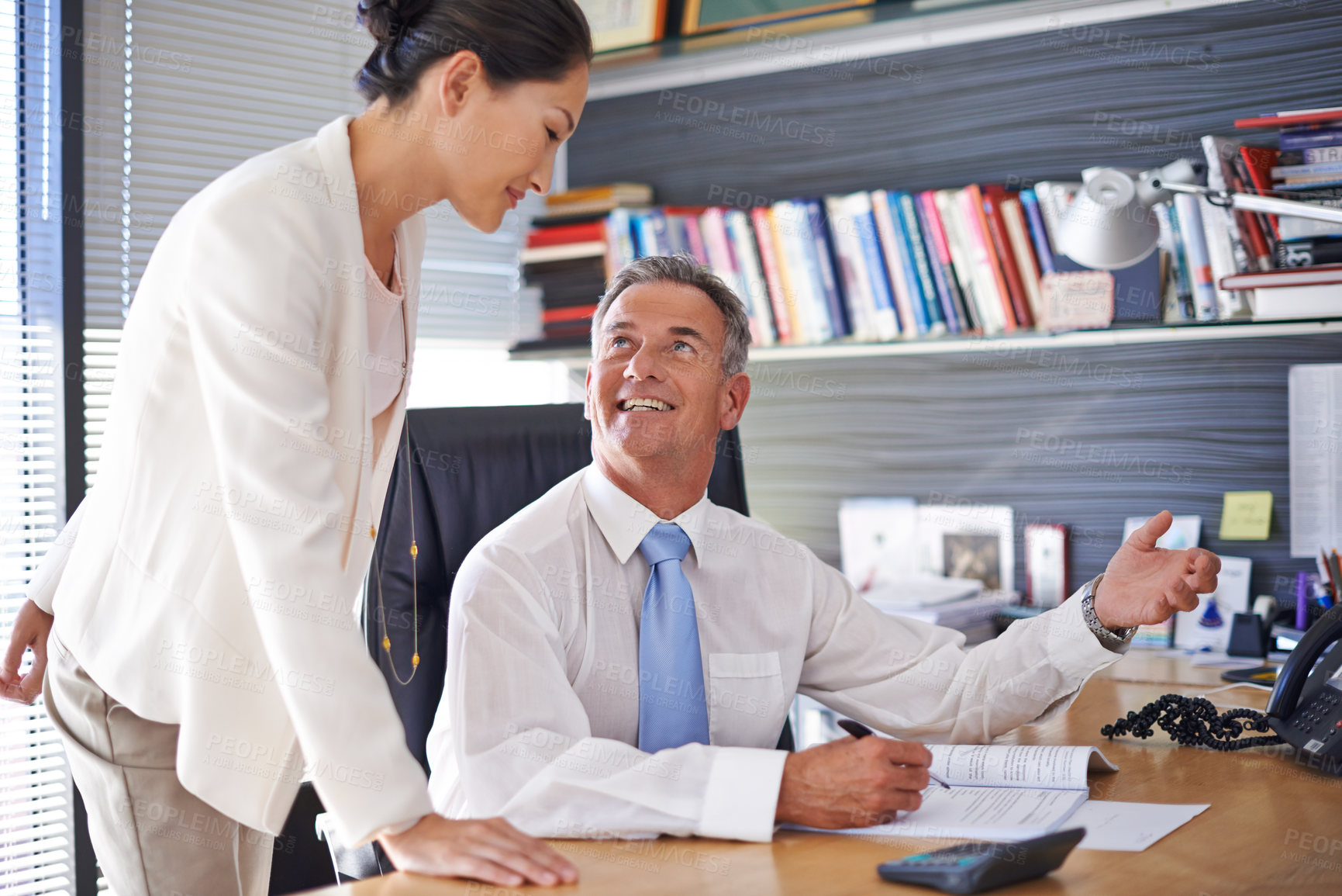 Buy stock photo Shot of a mature businessman talking to a female employee while sitting at his desk