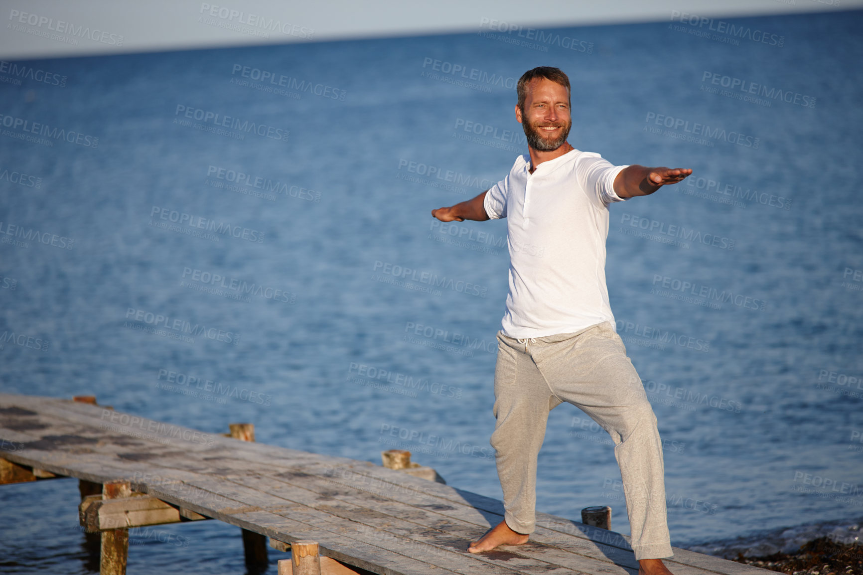 Buy stock photo Shot of a handsome mature man doing yoga beside the ocean