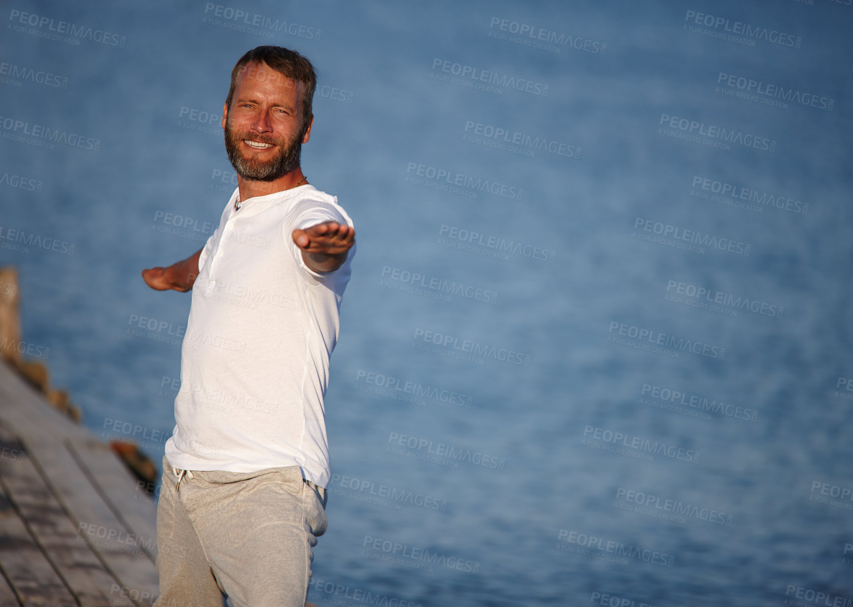 Buy stock photo Ocean, man and stretching on portrait for fitness, yoga and exercise in German. Male person, outdoor and smile or satisfied for retirement on break with self care, wellness or health with open arms