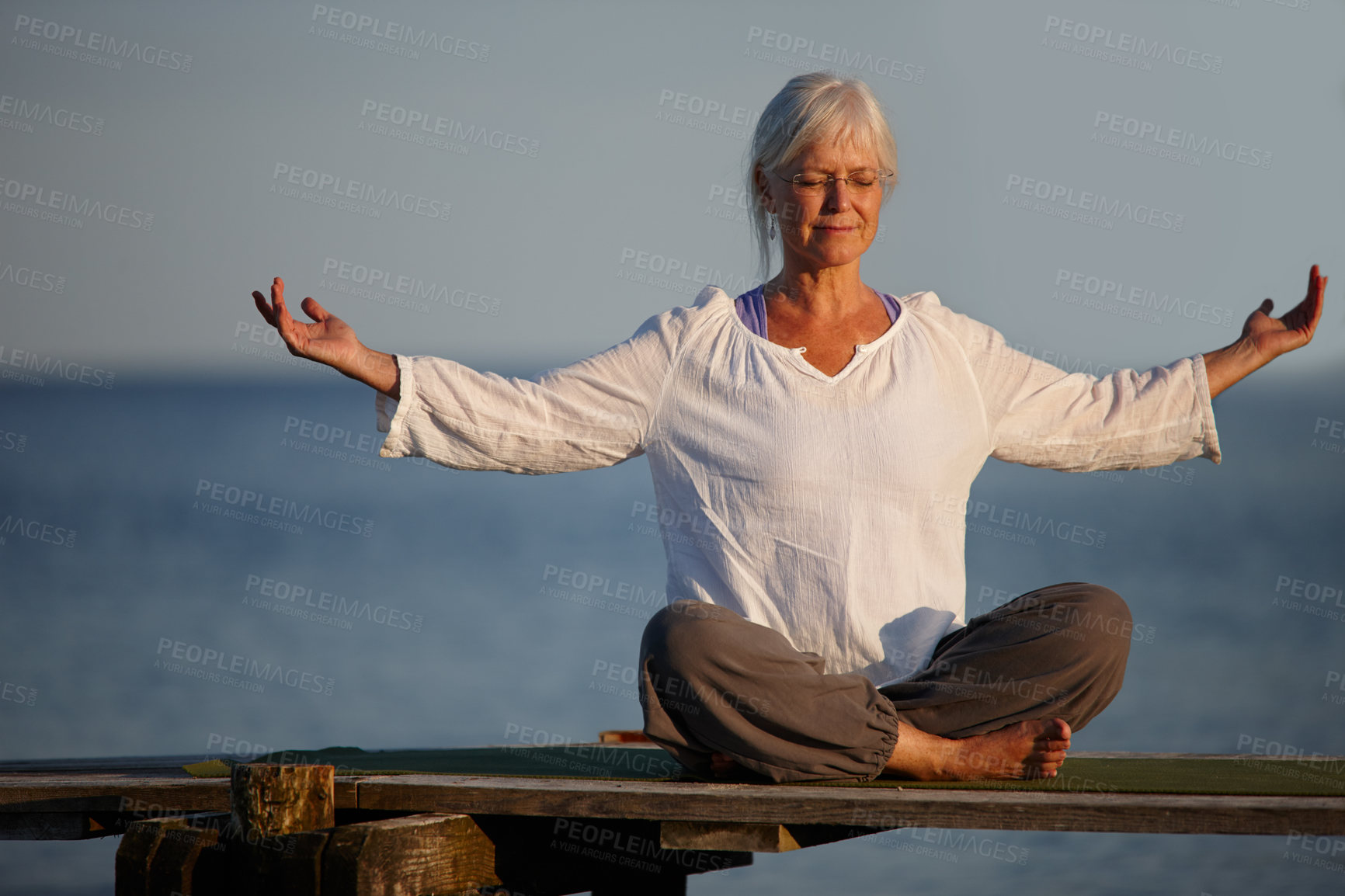 Buy stock photo Full length shot of an attractive mature woman doing yoga on a pier out on the ocean