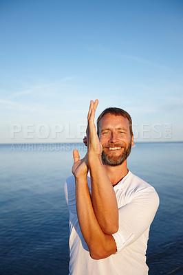 Buy stock photo Yoga, hands and portrait of man on beach with smile, health and wellness exercise in calm nature. Peace, stretching and person in eagle pose at ocean for fitness, balance and happy outdoor workout