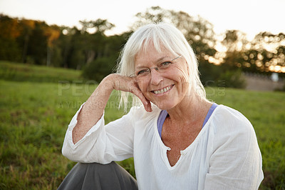 Buy stock photo Portrait of senior woman relaxing and sitting alone in a nature park outside at sunset. Smiling and happy elderly retired woman enjoying free time on weekend. One cheerful mature woman feeling free