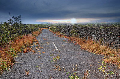 Buy stock photo Empty road through a field with burnt grass and cloudy sky with copy space. A curved countryside road or open asphalt roadway between dry land near Mauna Kea volcanic mountainside, Hawaii, Big Island