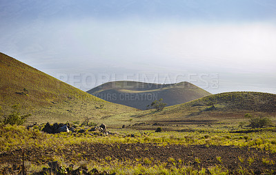 Buy stock photo High angle of a volcano crater against a mysterious cloudy horizon with copy space. View of undisturbed green nature scene of calm grass fields over a mountain and hiking trail in Mauna Loa in Hawaii