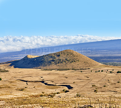 Buy stock photo Copy space with a volcano crater on a cloudy blue horizon. Empty barren nature scene of dry grass fields over a mountain and a hiking trail. High angle background of Mauna Loa in Hawaii