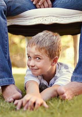 Buy stock photo Shot of a cute little boy lying on the grass underneath a chair which his father is sitting on