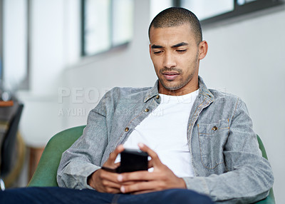 Buy stock photo Shot of a handsome young office worker using a cellphone while sitting in an office