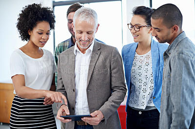 Buy stock photo Shot of a group of colleagues using a digital tablet while standing in an office