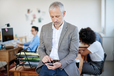 Buy stock photo Shot of a mature businessman using a cellphone while sitting on a table in an office