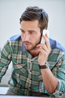 Buy stock photo Shot of a young designer talking on a cellphone at his desk