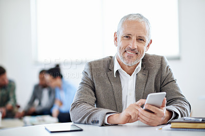 Buy stock photo Shot of a mature businessman using a cellphone while sitting at a table in an office