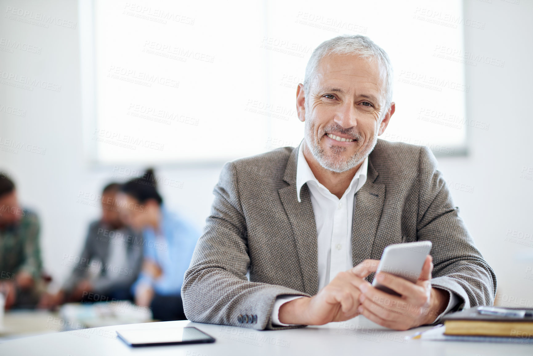 Buy stock photo Shot of a mature businessman using a cellphone while sitting at a table in an office
