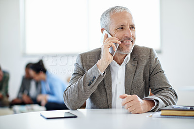 Buy stock photo Shot of a mature businessman talking on a cellphone while sitting at a table in an office