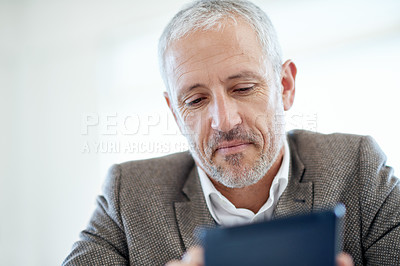 Buy stock photo Shot of a mature businessman using a digital tablet while sitting at a table in an office