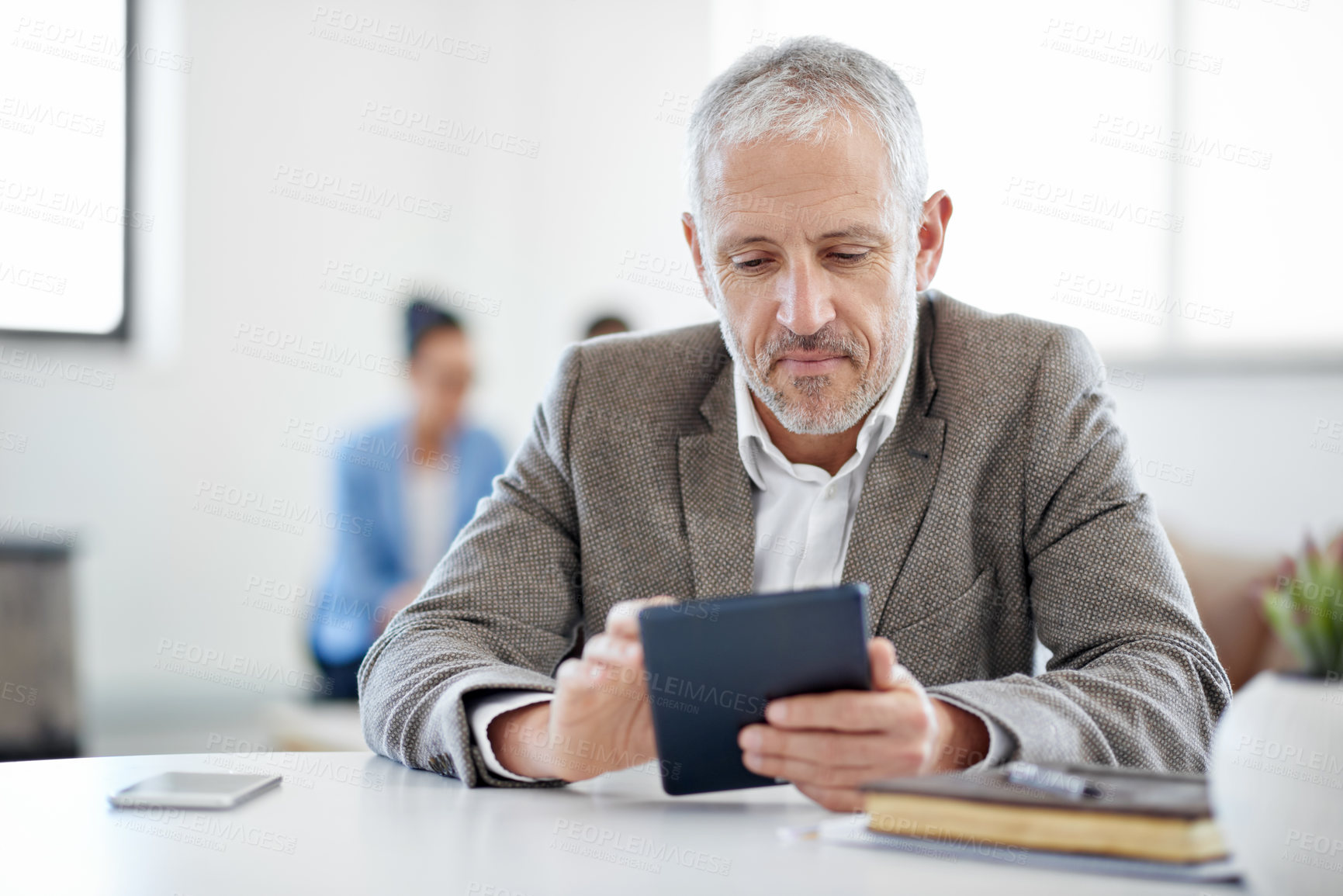 Buy stock photo Shot of a mature businessman using a digital tablet while sitting at a table in an office