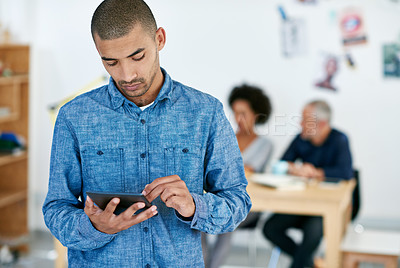 Buy stock photo Cropped shot of a young businessman using a tablet with his colleagues in the background. The commercial designs displayed  represent a simulation of a real product and have been changed or altered enough by our team of retouching and design specialists so that they don't have copyright infringements