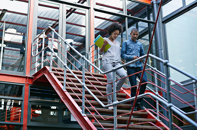 Buy stock photo Two colleagues walking side by side down stairs in their building