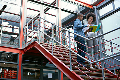 Buy stock photo Two colleagues walking side by side down stairs in their building