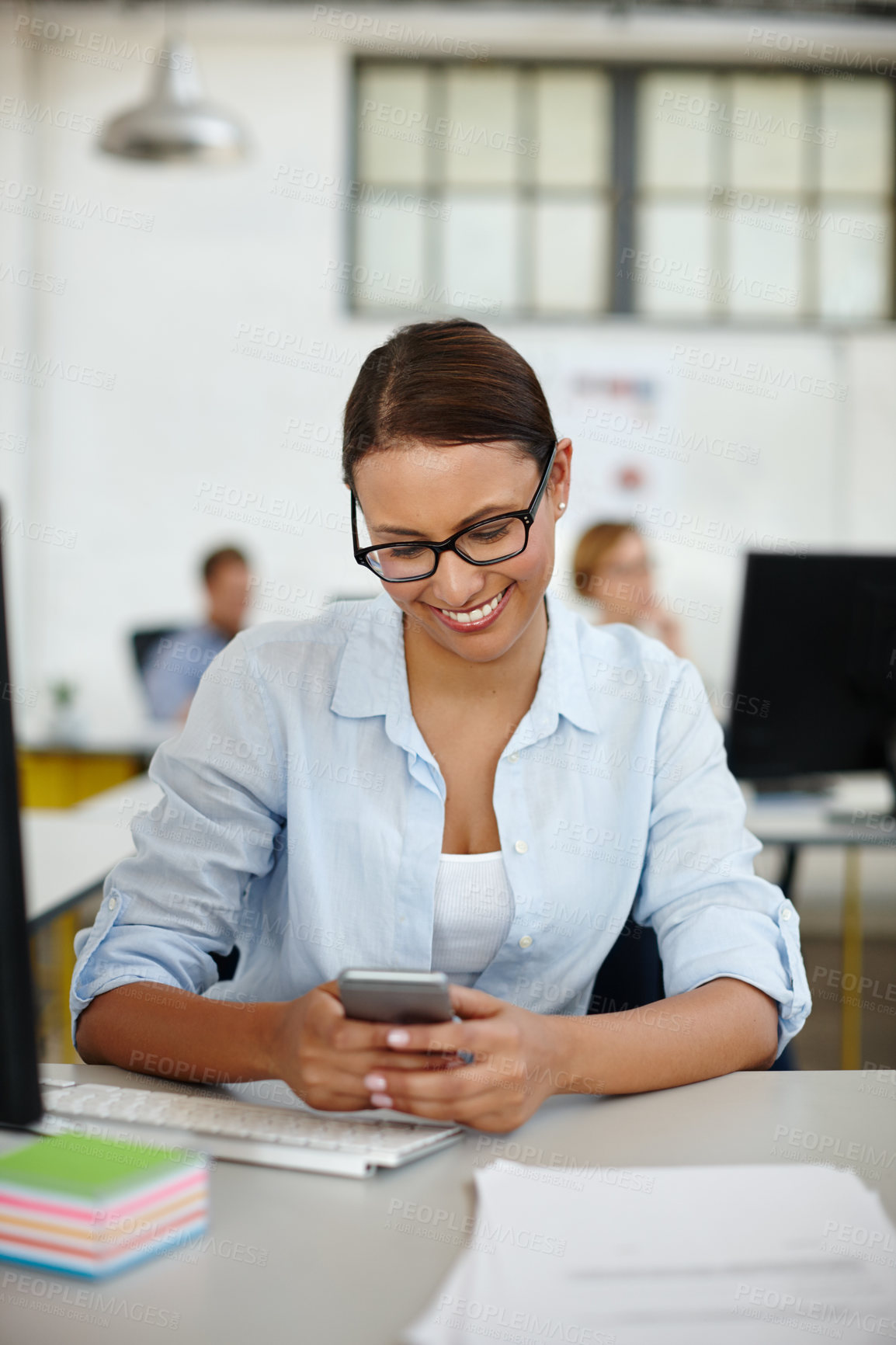 Buy stock photo Shot of a young female designer using her cellphone while sitting at her desk
