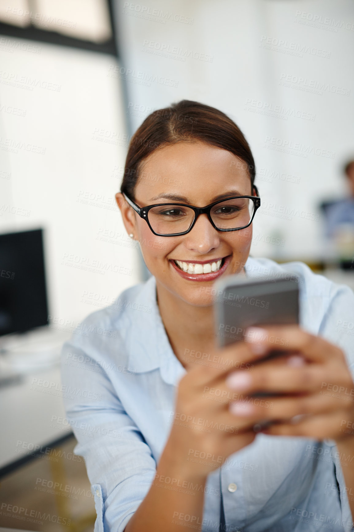 Buy stock photo Shot of a young woman smiling while using her cellphone at work